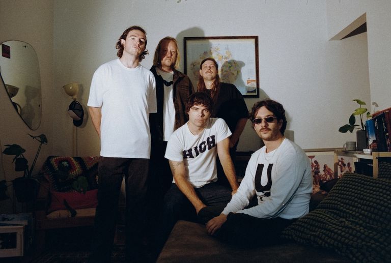 Indie rock band The Velvet Club posing indoors in a dimly lit room with vintage decor, captured in a grainy, film-style aesthetic.
